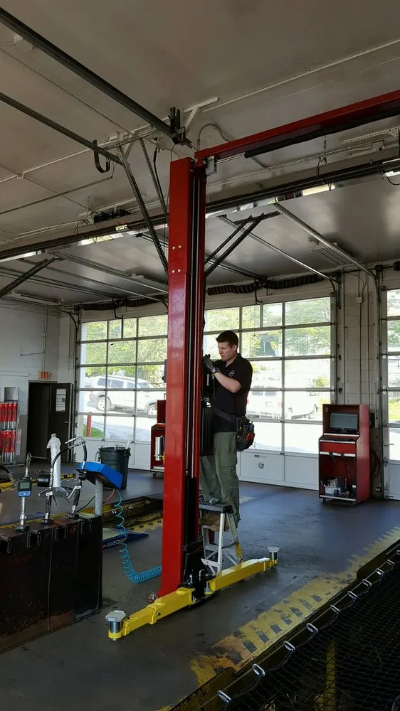 An electrician on a ladder in a service garage beside a vehicle lift