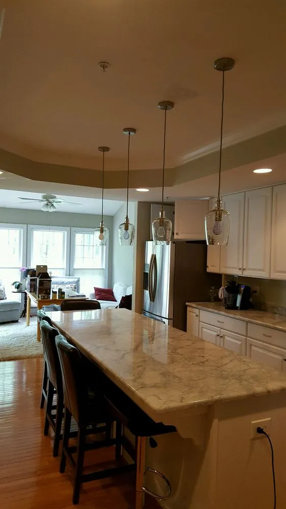 Three glass pendant lights over a granite kitchen island, with recessed lights in a tray ceiling