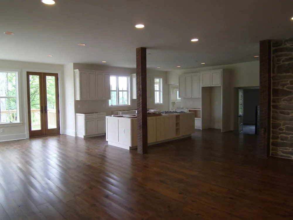 An open-plan renovated room with wide plank floors, a stone wall and evenly spaced recessed lights