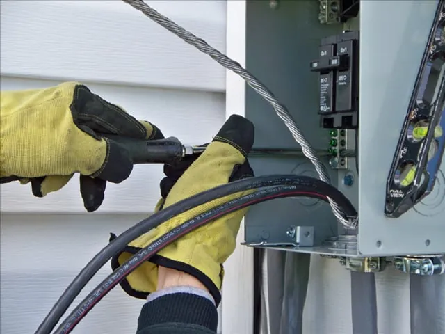 Gloved hands feeding cable into a panel on a house wall