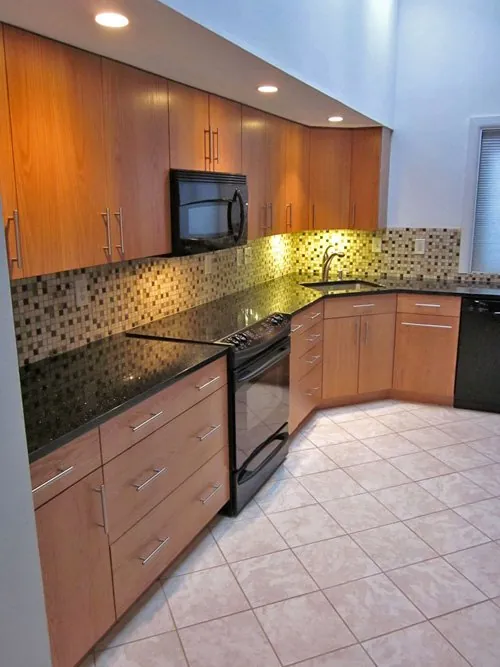 Under-cabinet lighting washing a mosaic backsplash and dark granite counter, with recessed lights above