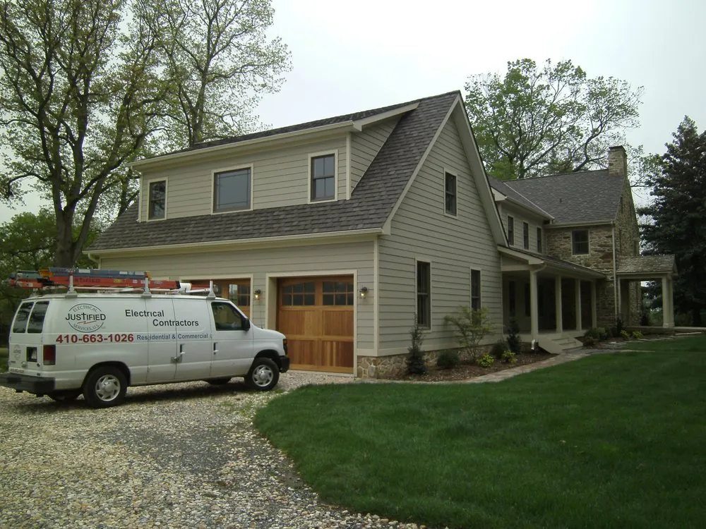 The white Justified Electrical van, lettered Electrical Contractors, Residential & Commercial, parked at a finished house with a new garage