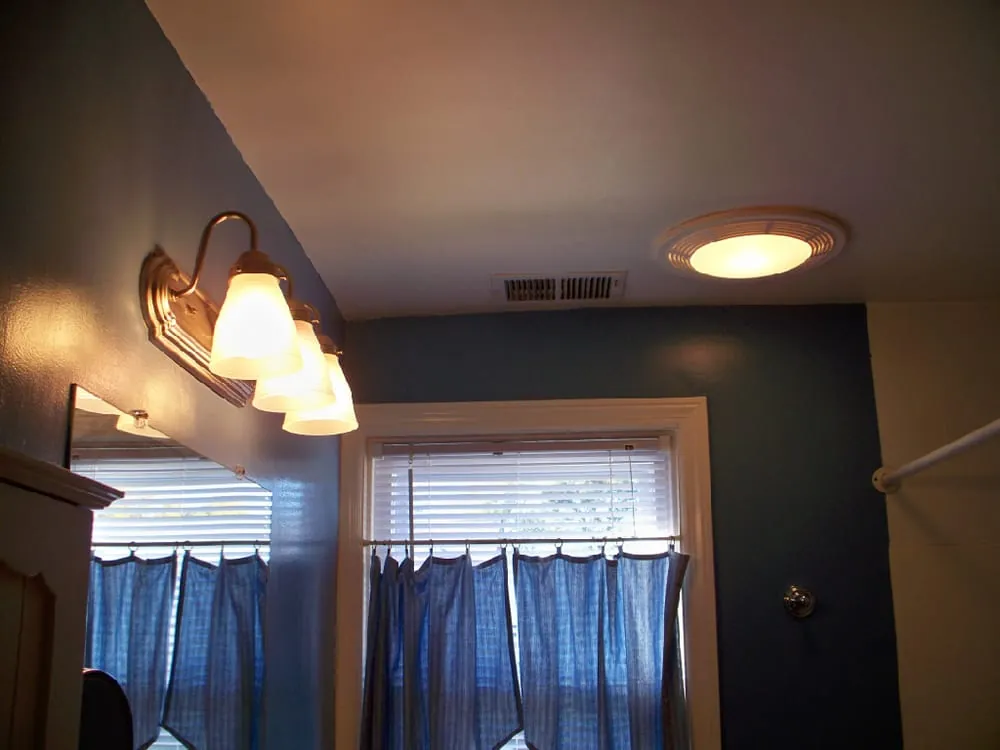 A three-light brass vanity fixture and a ceiling light in a navy blue bathroom